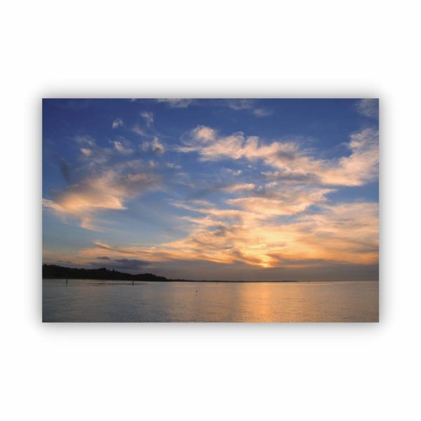 A photo wall art of a beautiful ocean view during sunset behind the clouds in a blue sky.