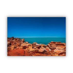 Beautiful photography of red rocks in Broome WA with blue sky and ocean water in the background.